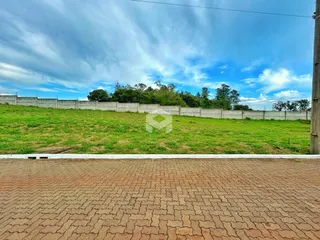 Vista externa de um terreno com cerca branca e vegetação verde.