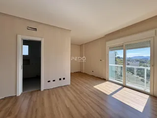 Interior de uma sala com piso de madeira e grandes janelas.