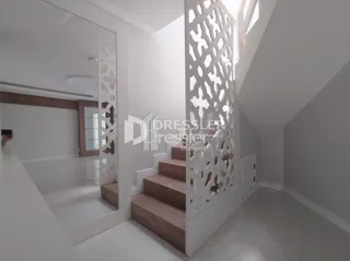 Interior de um corredor com escadaria decorativa em branco.