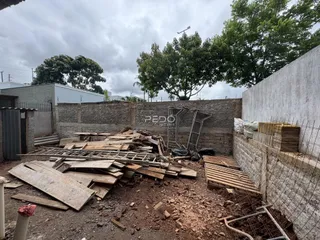 Vista externa de uma propriedade com muro e entulho no primeiro plano.