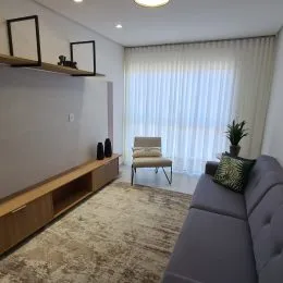 Sala de estar iluminada com cortinas brancas e um sofá cinza.