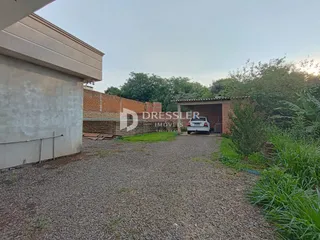 Vista externa de uma propriedade com muro de tijolos e área de acesso em cascalho.