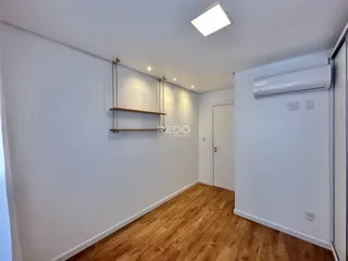 Uma vista interna de um corredor com piso de madeira clara e paredes brancas.