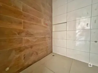 Uma parede revestida em tons de marrom claro e outra parede branca com azulejos compõem este ambiente.