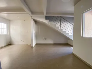 Vista interna de uma sala ampla com piso claro e escadaria moderna.
