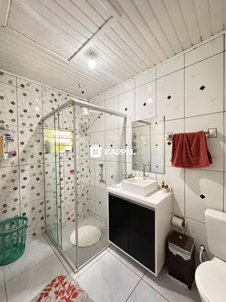 Banheiro com box de vidro e revestimento de azulejos brancos.
