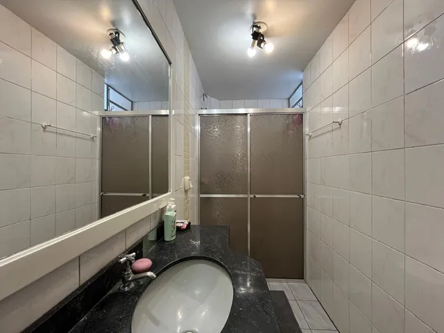 Banheiro com bancada escura e revestimento de azulejos brancos.