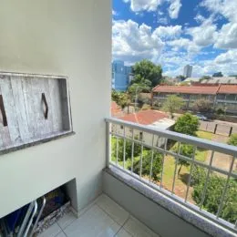 Vista externa de um balcão com vegetação e edifícios ao fundo.