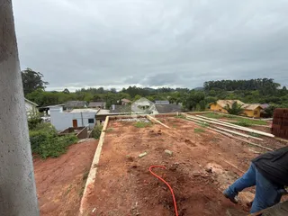 Vista de um terreno em terra vermelha com delimitações rudimentares no fundo.