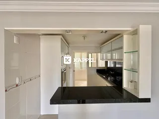 Vista interna da cozinha com armários brancos e bancadas escuras.