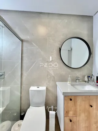 Foto de um banheiro com azulejos claros e um espelho redondo.