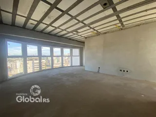 A foto mostra um espaço interno com teto de concreto aparente e grandes janelas.