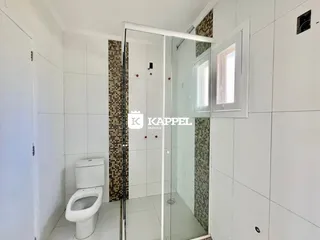 Banheiro com revestimento de azulejos brancos e marrons e box de vidro transparente.