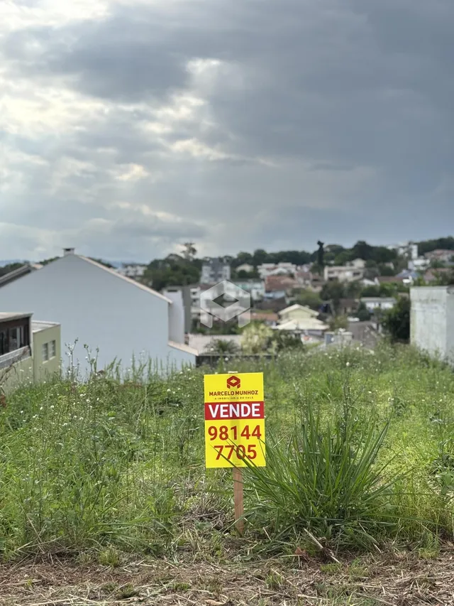 Vista externa de um terreno com grama alta e uma placa de venda.
