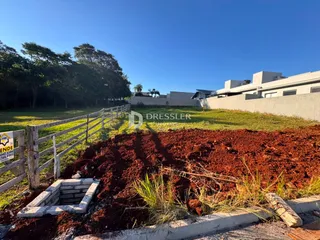 Vista externa de um terreno com cerca de madeira e solo avermelhado.