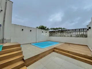Piscina externa com deck de madeira e muro branco.