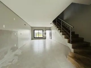 Vista interna de um espaço amplo com paredes brancas e um corredor que leva a uma escadaria.