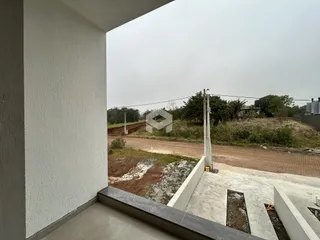 Vista externa de uma construção com área de terra e vegetação ao fundo.