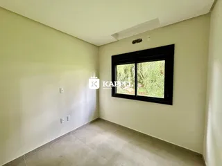 Ambiente interno com paredes claras e piso de cerâmica, mostrando uma janela com vista para a vegetação.