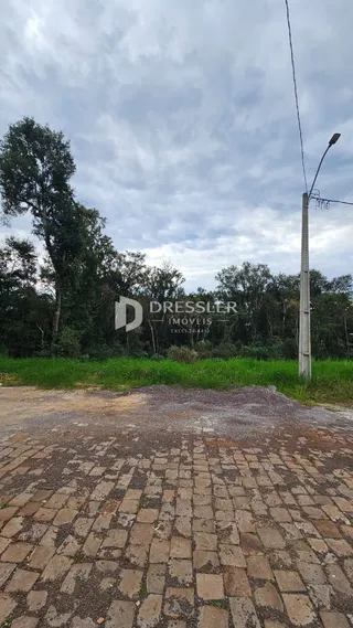 Vista externa de uma propriedade com área pavimentada e vegetação ao fundo.