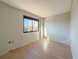 Ambiente interno de uma sala com piso de madeira clara e grande janela.