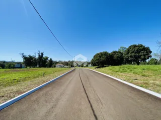 Vista de uma estrada rural com campos e árvores sob um céu azul claro.