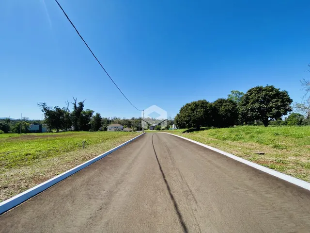 Vista de uma estrada rural com campos e árvores sob um céu azul claro.