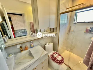Banheiro com bancada de mármore e box de vidro transparente.