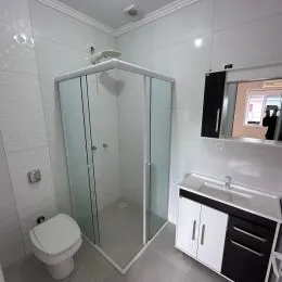 Interior de um box de banheiro com box de vidro e revestimento branco.