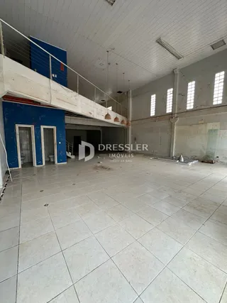 Vista interna de um espaço amplo com teto alto e piso de cerâmica.