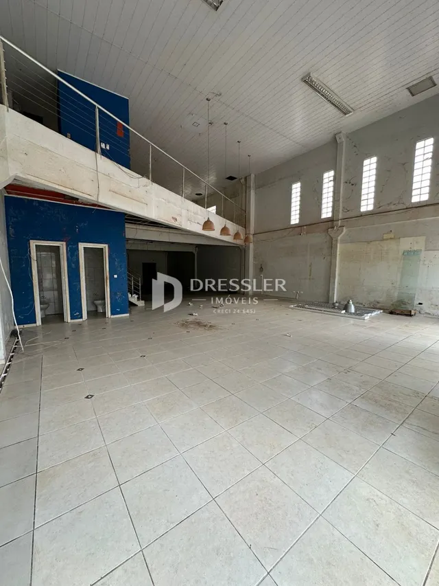 Vista interna de um espaço amplo com teto alto e piso de cerâmica.