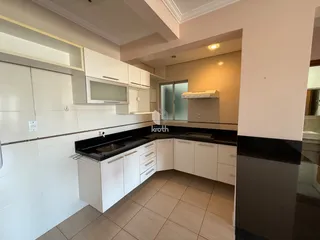 Foto da cozinha com armários brancos e bancadas escuras em um imóvel no Brasil.