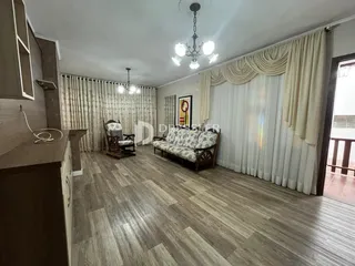 Sala de estar com piso de madeira clara e cortinas claras.