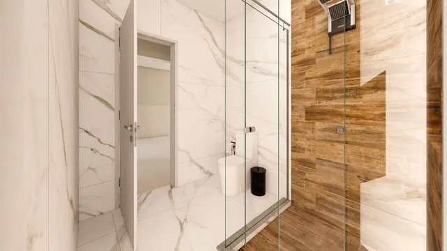 Banheiro com revestimento em mármore branco e box de vidro transparente.