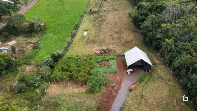 Vista aérea de uma propriedade rural com campos gramados e vegetação densa.