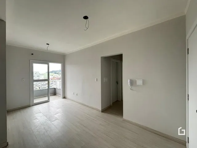 Ambiente interno de uma sala com piso de madeira clara e paredes brancas.