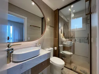 Banheiro moderno com bancada de mármore e box de vidro transparente.