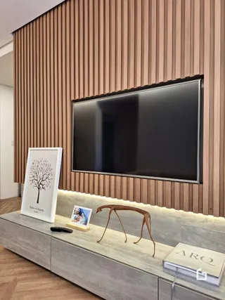 Sala com painel de madeira e televisão montada na parede.