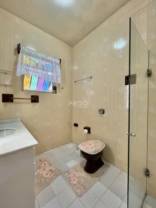 Banheiro com revestimento cerâmico e box de vidro.