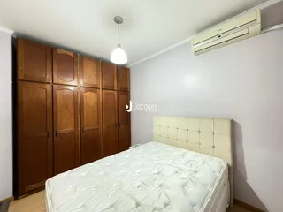 Quarto com armários de madeira e cama de cabeceira estofada.