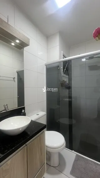 Foto do interior de um banheiro com box de vidro e revestimento branco.
