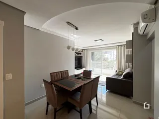 Ambiente de jantar com mesa de madeira e sala de estar integrada.