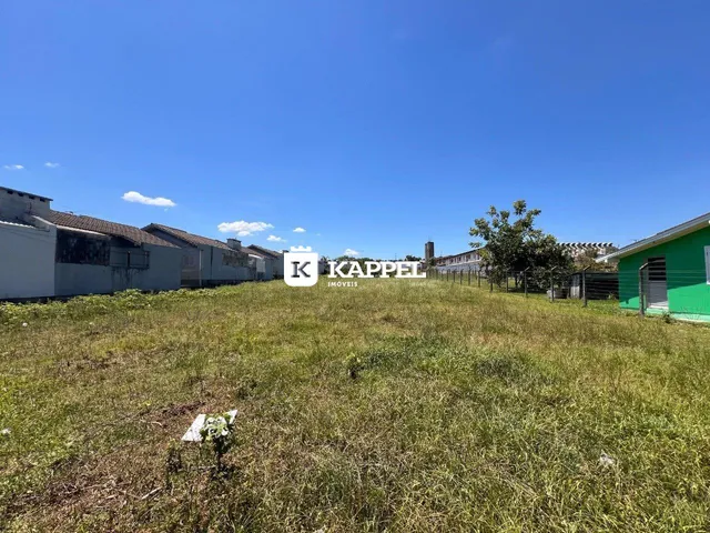 Vista externa de um terreno gramado com edificações ao fundo sob céu azul.