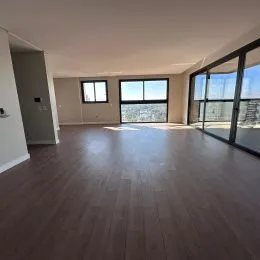 Sala de estar com piso de madeira clara e grandes janelas.