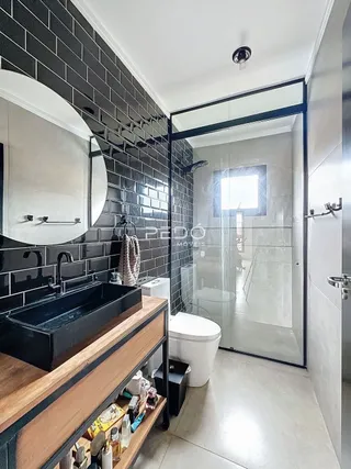 Banheiro moderno com revestimento de azulejos pretos e box de vidro transparente.