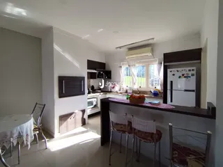 Ambiente interno de uma cozinha e sala de jantar com piso claro e armários escuros.