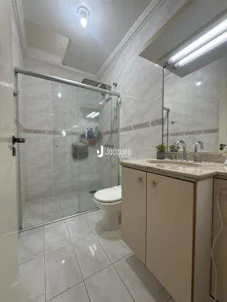 Banheiro com box de vidro e revestimento cerâmico claro.