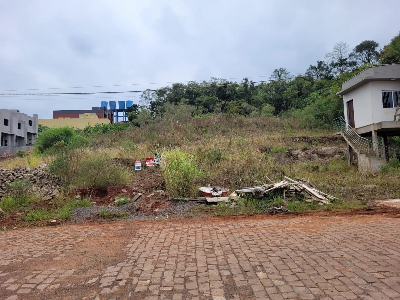 Vista externa de um terreno com vegetação seca e uma estrutura de construção ao fundo.