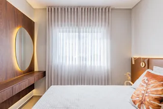 Quarto com cabeceira de madeira e cortinas claras.