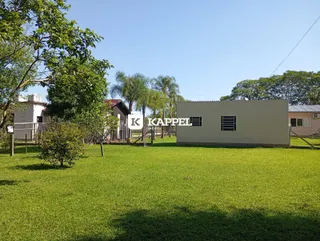 Vista externa de uma propriedade com gramado verde e vegetação ao fundo.